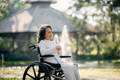 Asian elderly woman sitting on wheelchair outdoor in park relax your mind. Nursing home hospital garden concept.