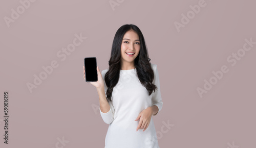Beautiful Asian woman holding smartphone mockup of blank screen on isolated brown background