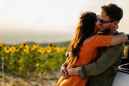 Beautiful young couple in love hugs and cuddles, sunflowers field background, travel and luxury holiday concept