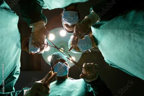 surgeon team standing above unite teamwork. medical group wearing uniform working together from patient view. surgical group above patient empower by stick tools together for success operate surgery