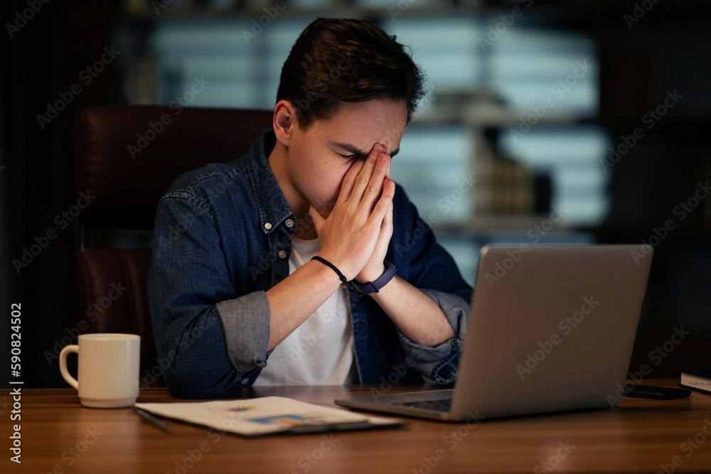 Tired man sitting in front of computer at dark office Tired man sitting in front of computer at dark office