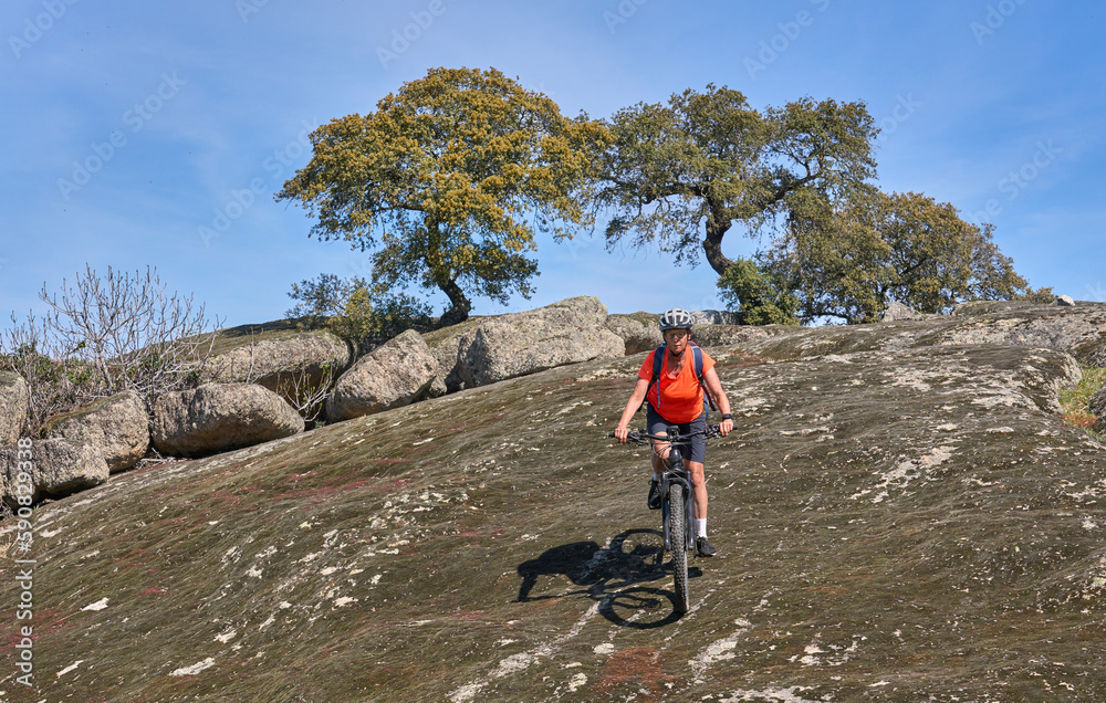 nice senior woman cyling with her electric mountain bike in a stone oak forest of the Extremadura department of Spain