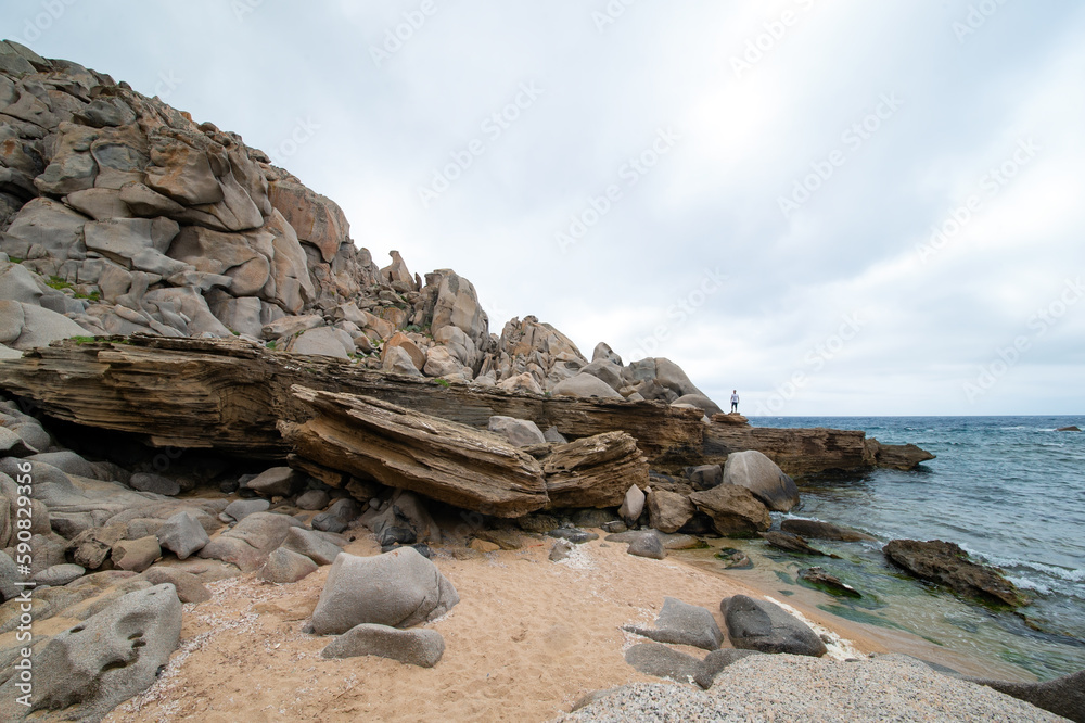 Stunning view of a person on some rocks in Valle della Luna. Cala Grande is located in the western part of the promontory of Capo Testa, in the territory of Santa Teresa Gallura, Sardinia, Italy.