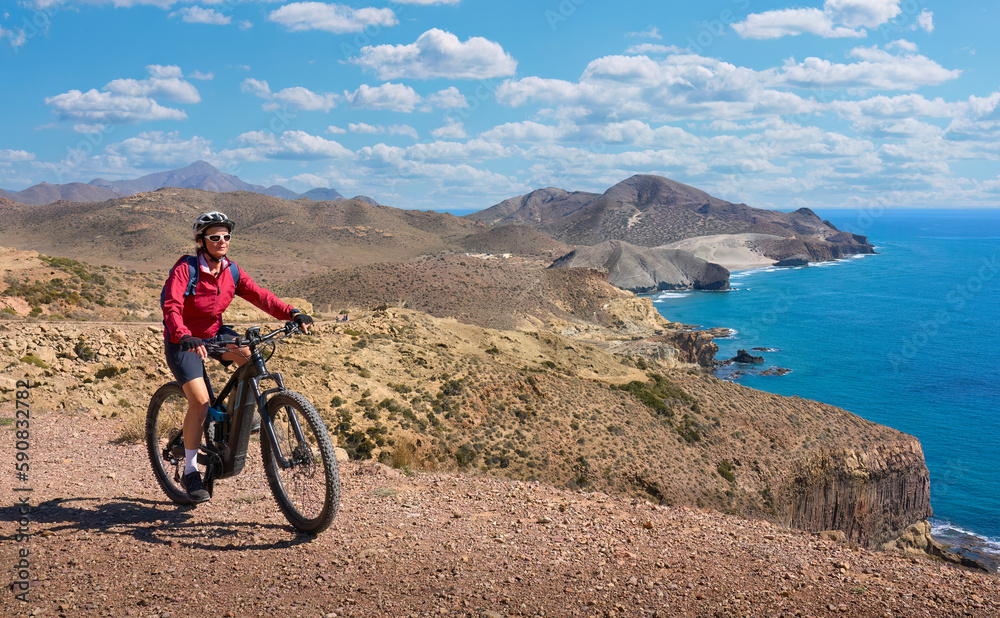 nice senior woman cycling with her electric mountain bike in the volcanic nature park of Cabo de Gata, Costa del Sol, Andalusia