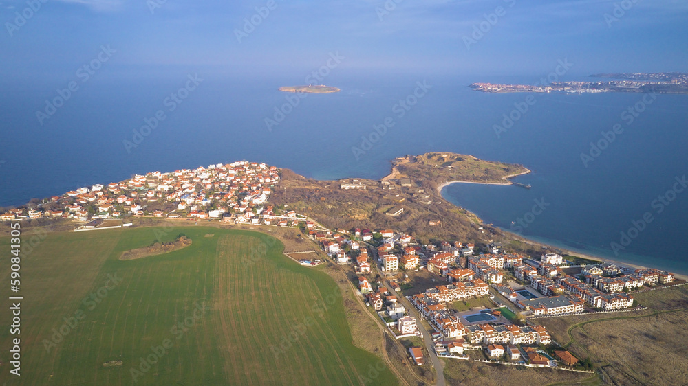 Obraz premium Top view from a drone on a small town with houses, among the field and on the horizon a clear blue sky and sea