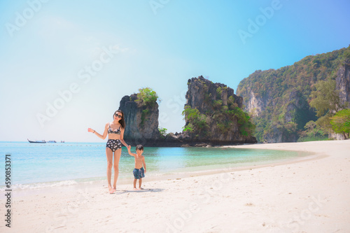 Boy and his mother are strolling along the beach, admiring the stunningly bright blue waters of Krabi, Thailand