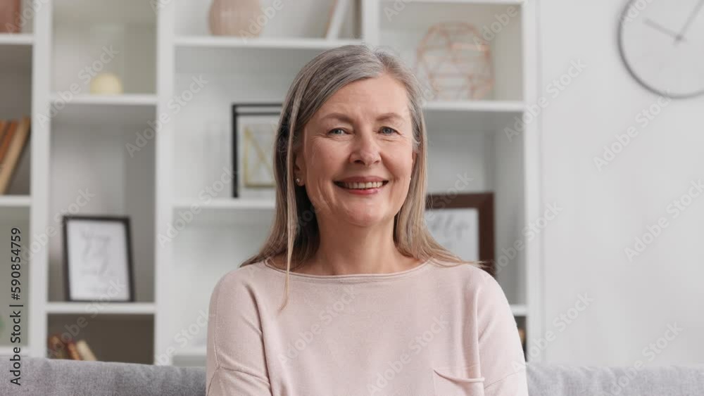 Happy senior woman sitting on sofa in nice apartment. A grayhaired grandmother in her 50s or 60s is resting on the couch at home, smiling. Happy senior woman sitting on sofa in nice apartment. A grayhaired grandmother in her 50s or 60s is resting on the couch at home, smiling.