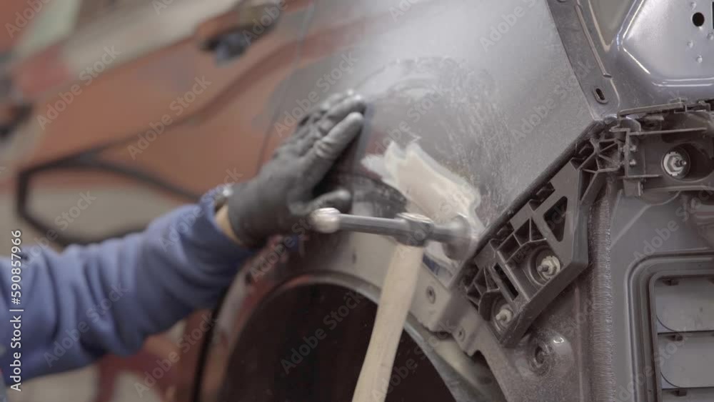 Car body repairer wearing protective gloves, working with a hammer on a car's sheet metal to repair it. Car body repairer wearing protective gloves, working with a hammer on a car's sheet metal to repair it.
