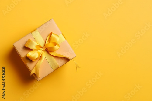 Gift box with golden satin ribbon and bow on yellow background. Holiday gift with copy space. Birthday or Christmas present, flat lay, top view. Christmas giftbox concept. AI generated.