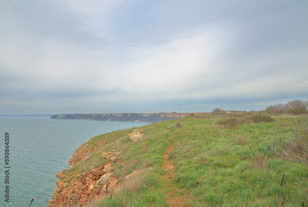 Turquoise sea and a rock with a green glade against the background of heavy rain clouds in early spring Turquoise sea and a rock with a green glade against the background of heavy rain clouds in early spring
