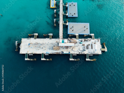 A bird's eye view of a ship navigating fishing boats moored to the docks, with village houses sprawling between the harbor
