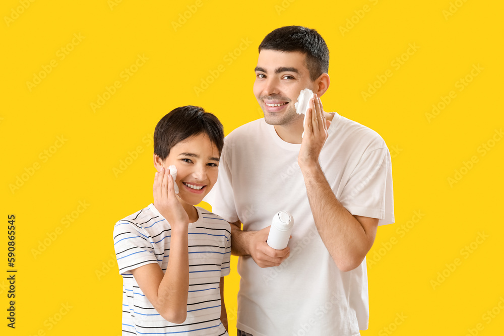 Man and his little son applying shaving foam onto faces against yellow background Man and his little son applying shaving foam onto faces against yellow background