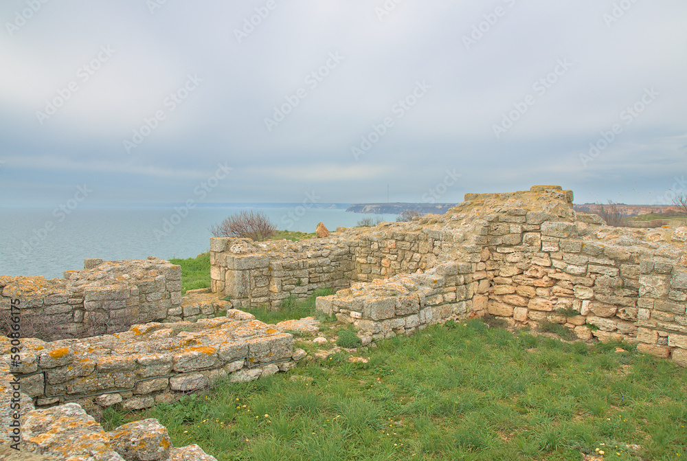 Turquoise sea and a rock with a green glade against the background of heavy rain clouds in early spring