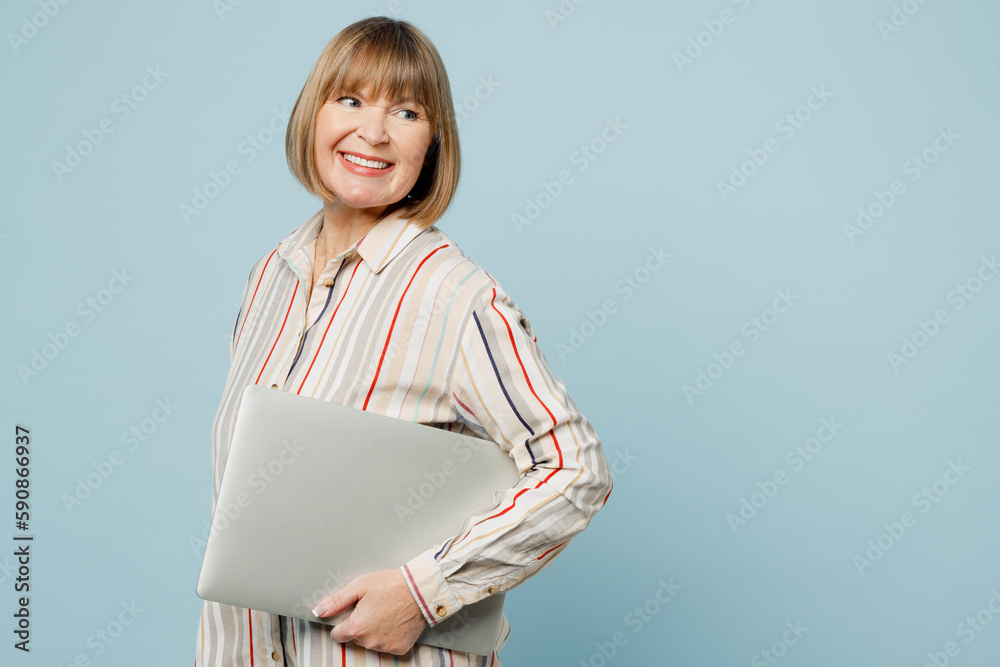 Obraz premium Profile elderly happy fun IT woman 50s years old wearing light striped shirt hold use work on laptop pc computer look aside on area isolated on plain pastel light blue cyan background studio portrait.