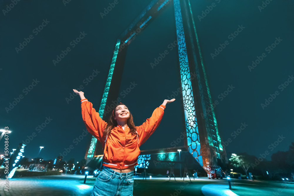 As the sun sets, the Dubai frame comes alive with colorful lights, making for a perfect backdrop for this smiling young woman.