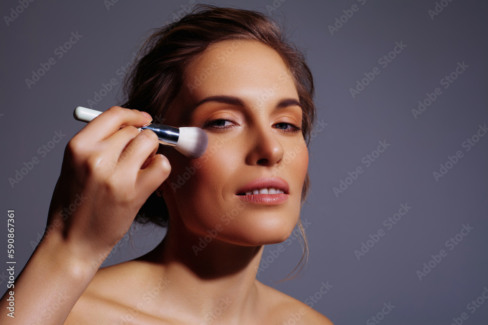 Correcting makeup with brush on face of beautiful blonde woman on gray background Correcting makeup with brush on face of beautiful blonde woman on gray background