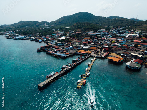 A bird s eye view of a ship navigating fishing boats moored to the docks  with village houses sprawling between the harbor 