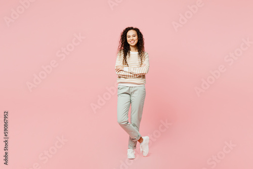 Full body smiling happy cheerful young woman of African American ethnicity she wear light casual clothes hold hands crossed folded look camera isolated on plain pastel pink background studio portrait.