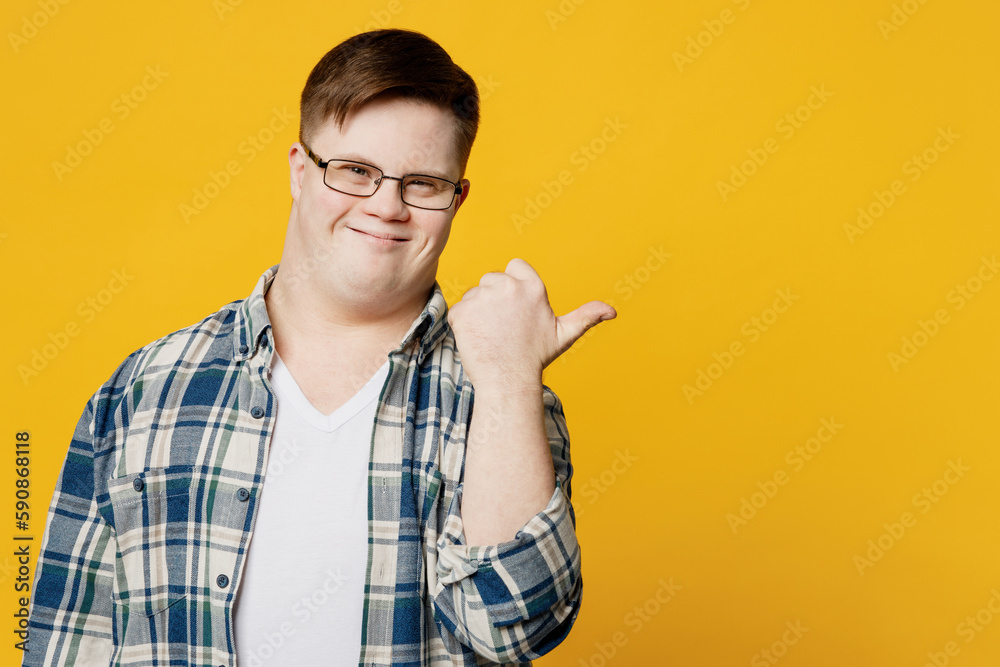 Young fun man with down syndrome wears glasses casual clothes point thumb finger aside on area workspace copy space isolated on pastel plain yellow color background. Genetic disease world day concept. Young fun man with down syndrome wears glasses casual clothes point thumb finger aside on area workspace copy space isolated on pastel plain yellow color background. Genetic disease world day concept.