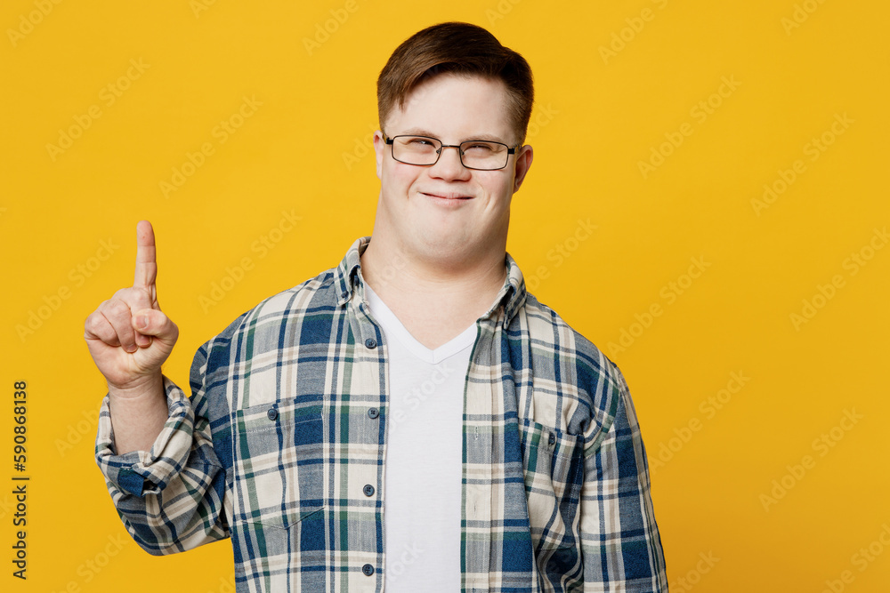Young fun smiling man with down syndrome wearing glasses casual clothes holding index finger up with great new idea isolated on pastel plain yellow color background. Genetic disease world day concept. Young fun smiling man with down syndrome wearing glasses casual clothes holding index finger up with great new idea isolated on pastel plain yellow color background. Genetic disease world day concept.