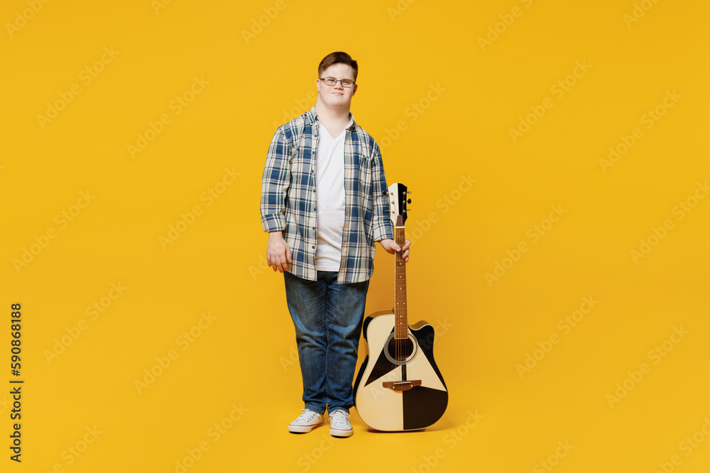 Full body young smiling happy man with down syndrome wear glasses casual clothes play guitar sing song look camera isolated on pastel plain yellow color background. Genetic disease world day concept. Full body young smiling happy man with down syndrome wear glasses casual clothes play guitar sing song look camera isolated on pastel plain yellow color background. Genetic disease world day concept.