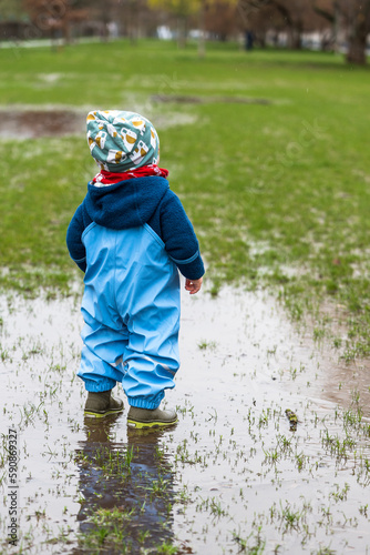 Fototapeta Naklejka Na Ścianę i Meble -  A little child standing in a puddle in a park during rainy weather