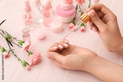 Female hands with bottle of cuticle oil  cosmetics and carnation flowers on color tile background  closeup