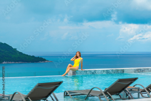 Beautiful young woman in swimwear relaxes in infinity pool at a luxury spa resort, enjoying the stunning sea view. A perfect summer vacation getaway.