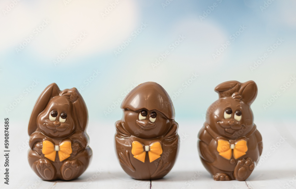 Chocolate Easter hares and a chicken in a shell on a light background.