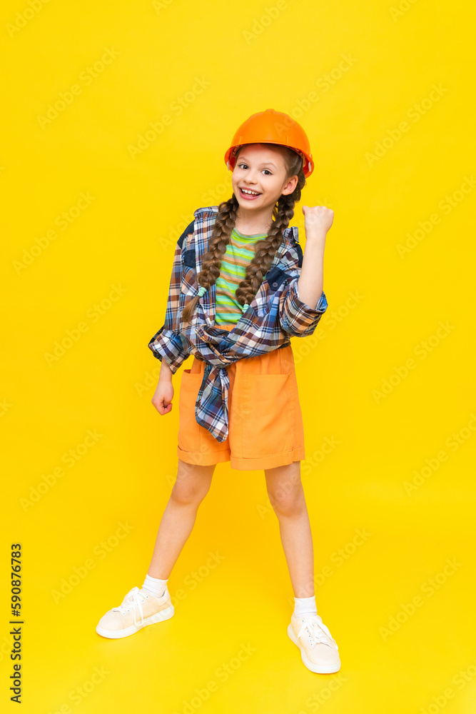 A child in a construction helmet. A little teenage girl rejoices at the upcoming renovation in the children's room. The profession of an engineer for a child. Yellow isolated background. A child in a construction helmet. A little teenage girl rejoices at the upcoming renovation in the children's room. The profession of an engineer for a child. Yellow isolated background.
