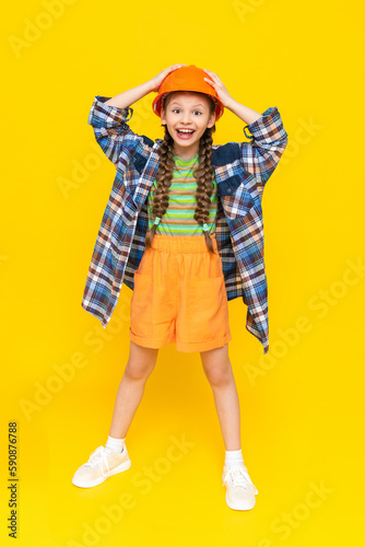 A child in a construction helmet. A little teenage girl rejoices at the upcoming renovation in the children's room. The profession of an engineer for a child. Yellow isolated background.