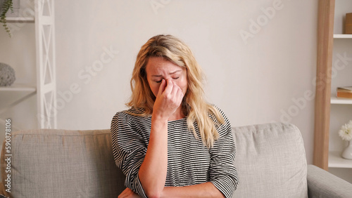 Upset news. Sorrowful situation. Crying woman. Sad despair lady bursting tears covering face hand sitting sofa in light room interior.