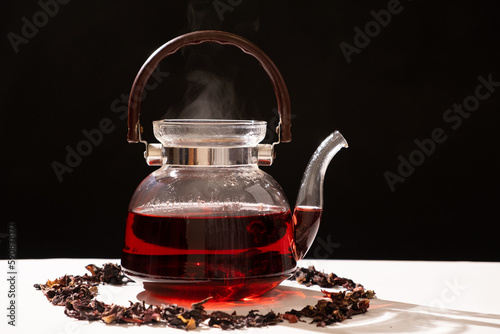 Red hibiscus tea from the petals of a Sudanese rose in a glass teapot, steam from a teapot on a black background