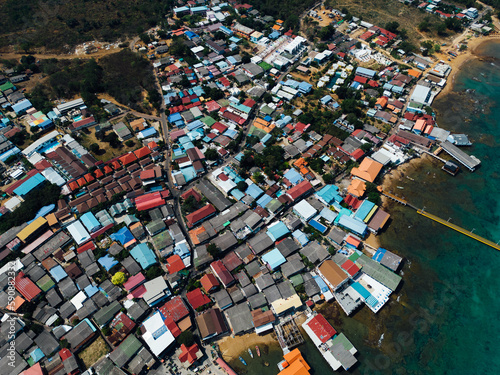 A bird's eye view of a ship navigating fishing boats moored to the docks, with village houses sprawling between the harbor
