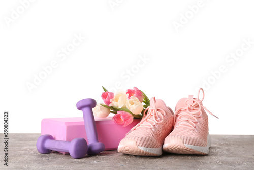 Sneakers with tulips, block and dumbbells on table against white background