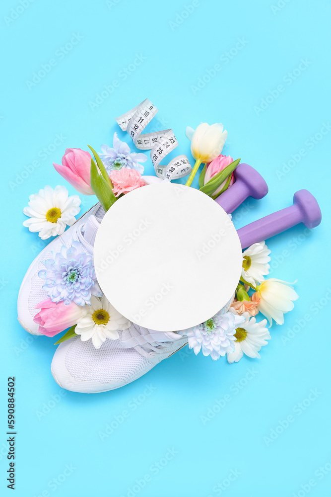 Blank card with sneakers, dumbbells, tape measure and spring flowers on blue background
