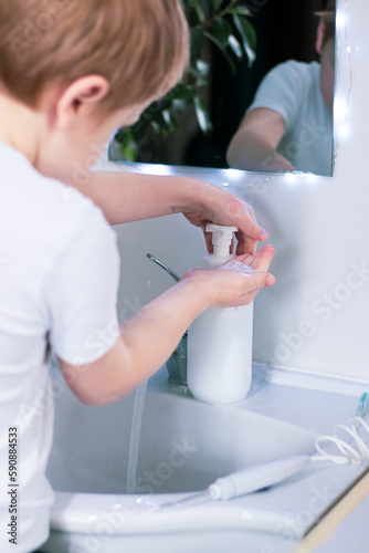 child boy in white T-shirt washing hands with liquid soap in the sink . Hygiene and healthy lifestyle concept