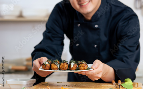 Selective focus making Japanese takoyaki street food, smiling with confidence, standing in kitchen. Restaurant, Hotel Concept.