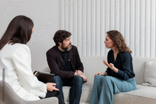 Concept of marital therapy. A female psychologist sits with her back to the camera and listens to the quarrel of a married couple during a therapy session