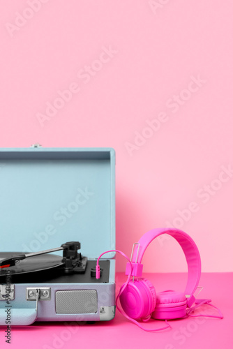 Record player with vinyl disk and headphones on table near pink wall