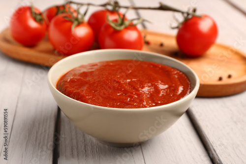 Bowl with tasty tomato paste on light wooden background, closeup