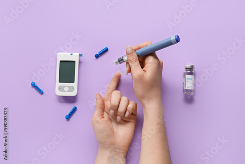Woman using lancet pen on lilac background. Diabetes concept