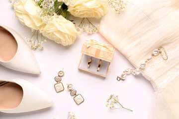 Box with wedding rings, jewelry, heels, flowers and dress on white background