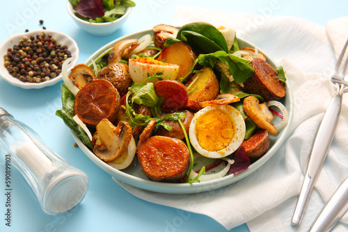 Plate of tasty potato salad with eggs and mushrooms on light blue background