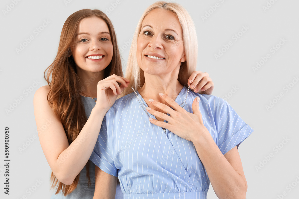 Young woman putting necklace around her mother's neck on grey background Young woman putting necklace around her mother's neck on grey background