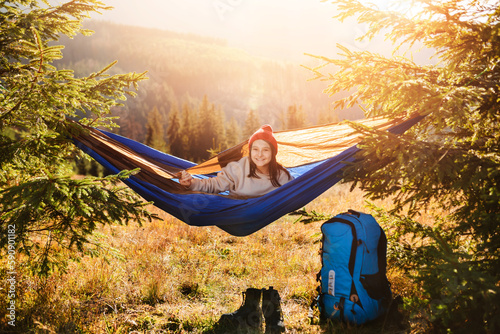 Teenage child lies in tourist hammock on a mountain landscape background. Sunny summer day.