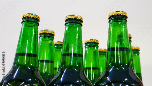 Close-up of many beautiful green glass bottles of beer with golden caps on a store shelf