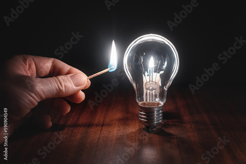 Power failure. A hand with a burning match in complete darkness next to a light bulb. Blackout in the city, power outage, energy crisis or blackout. Rising electricity prices for home and industry