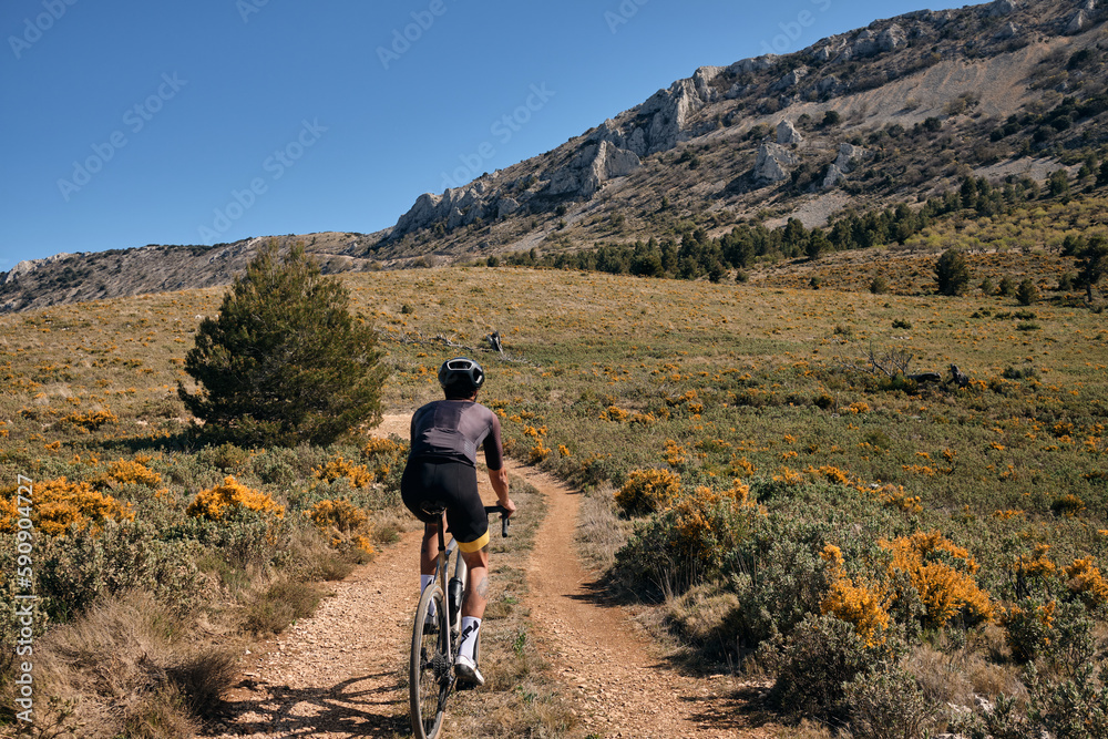 Man riding gravel bike on gravel road in mountains with scenic view.Cyclist riding on gravel bike.Cyclist practicing on gravel road.Man cyclist wearing cycling kit and helmet.Alicante region in Spain.