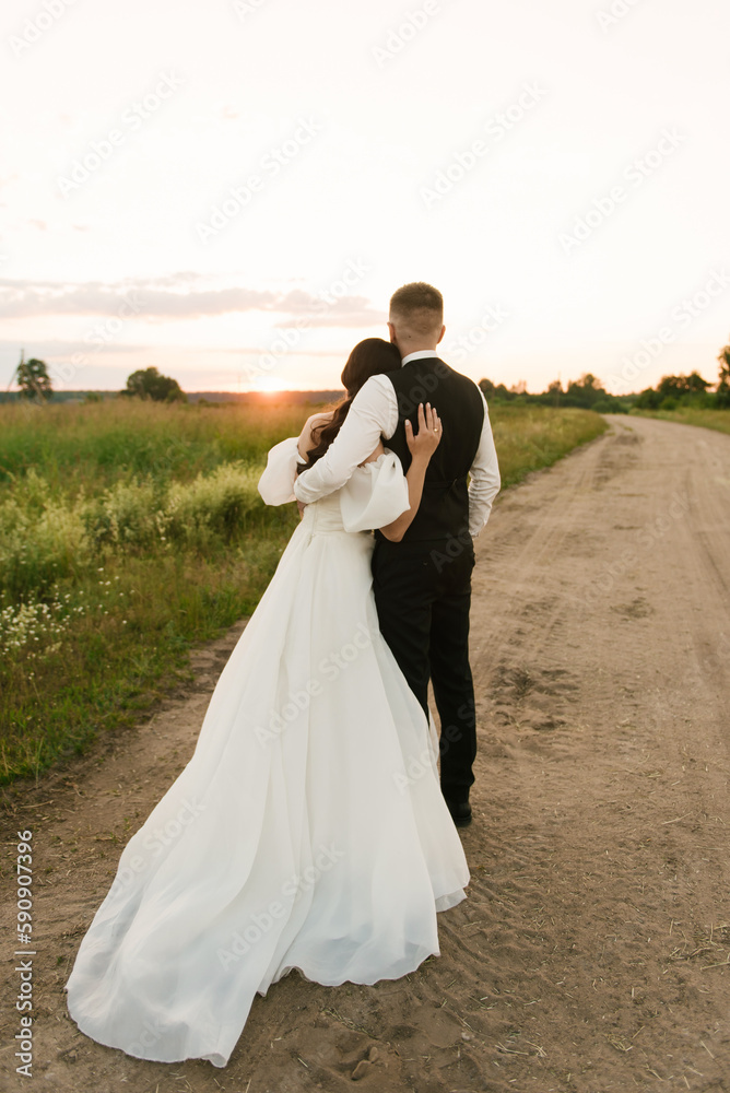 the bride and groom embrace, stand with their backs to the sunset